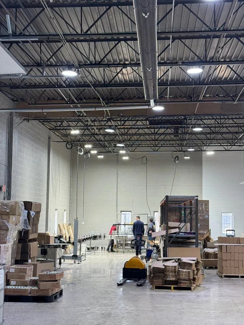 A warehouse interior lit by rows of LED high bay fixtures, with pallets and boxes on the floor