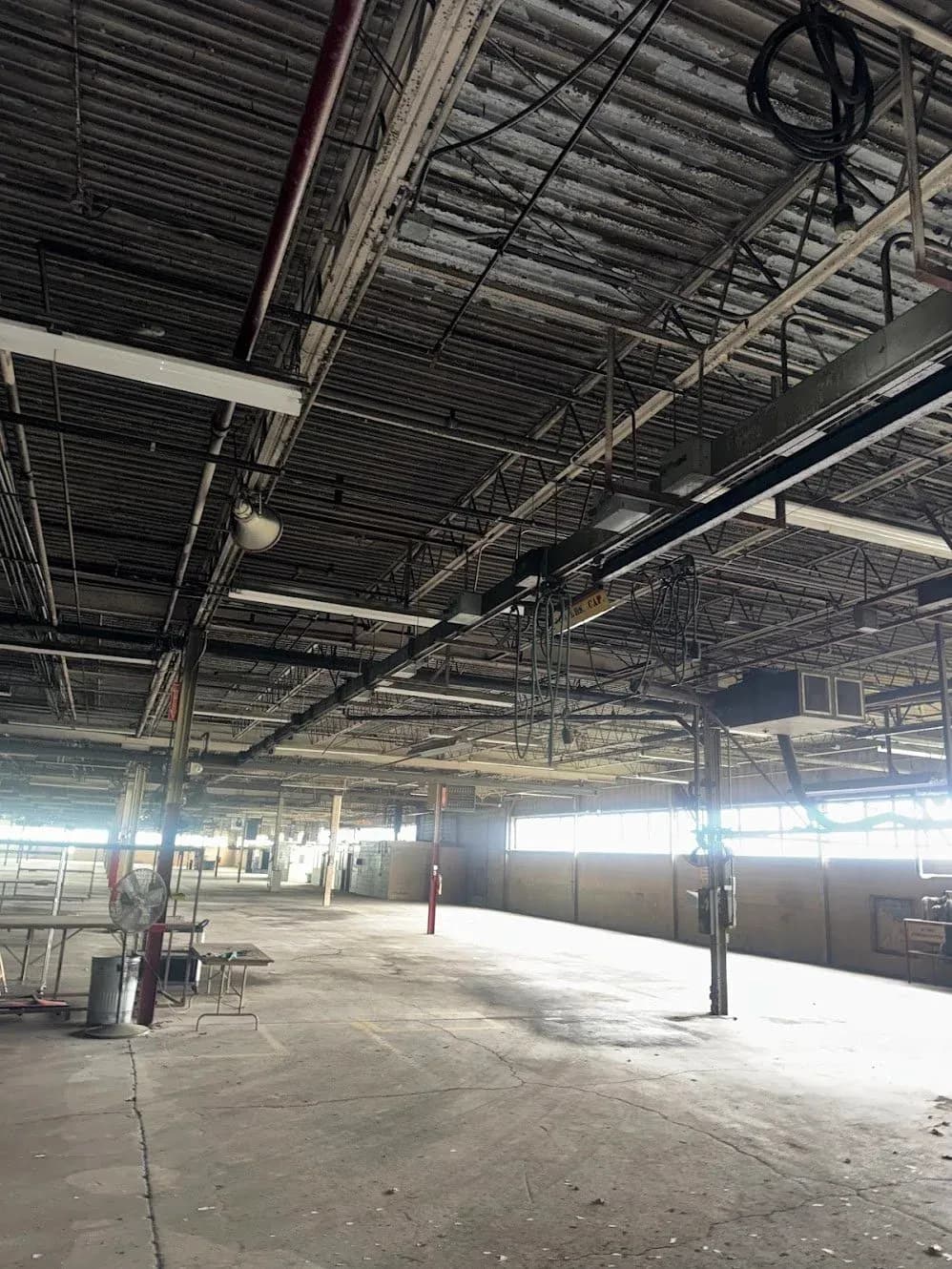 A large industrial building interior with heavy conduit and electrical runs across the ceiling
