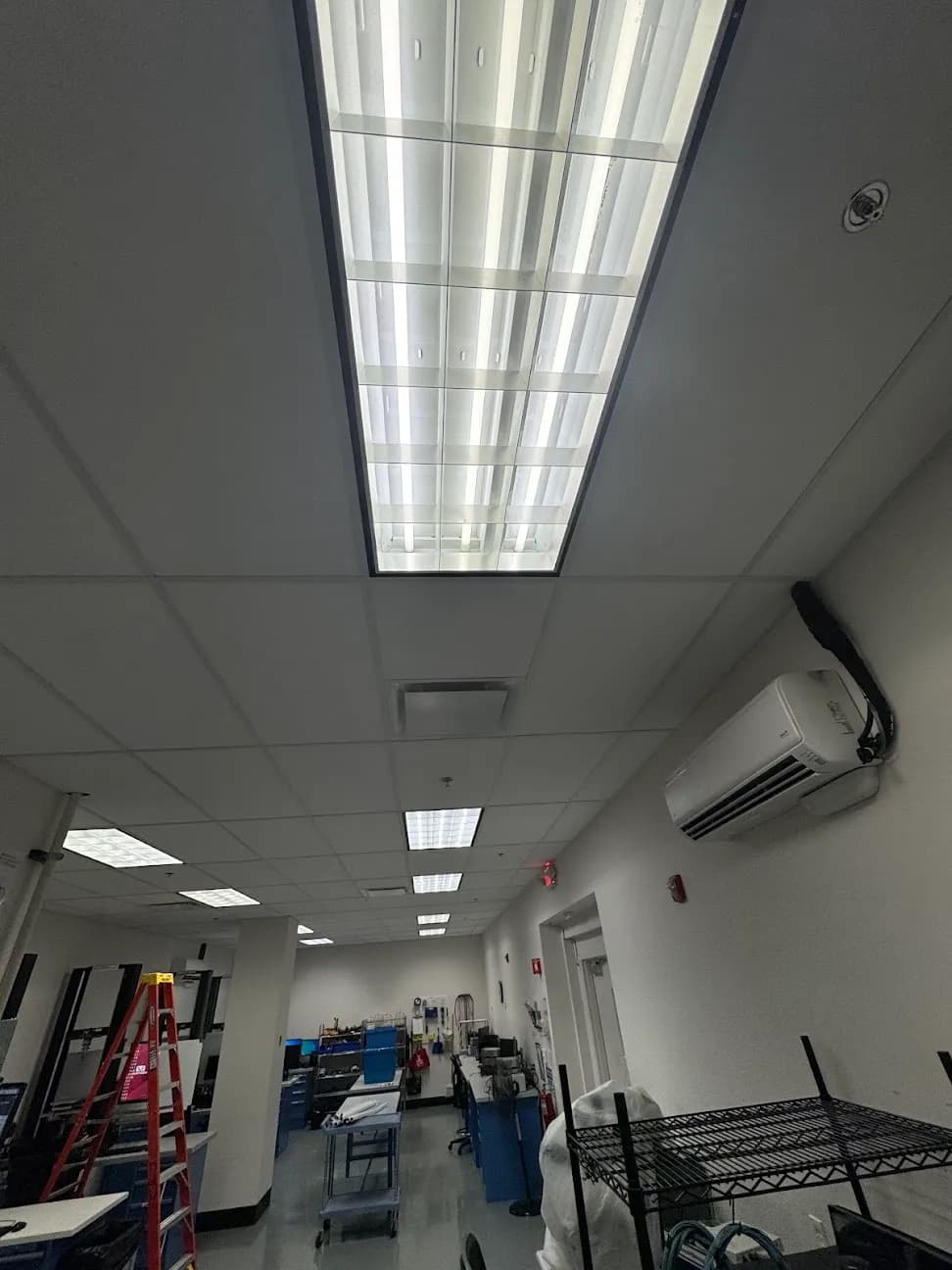 An office corridor with recessed ceiling light panels and a wall-mounted mini split unit