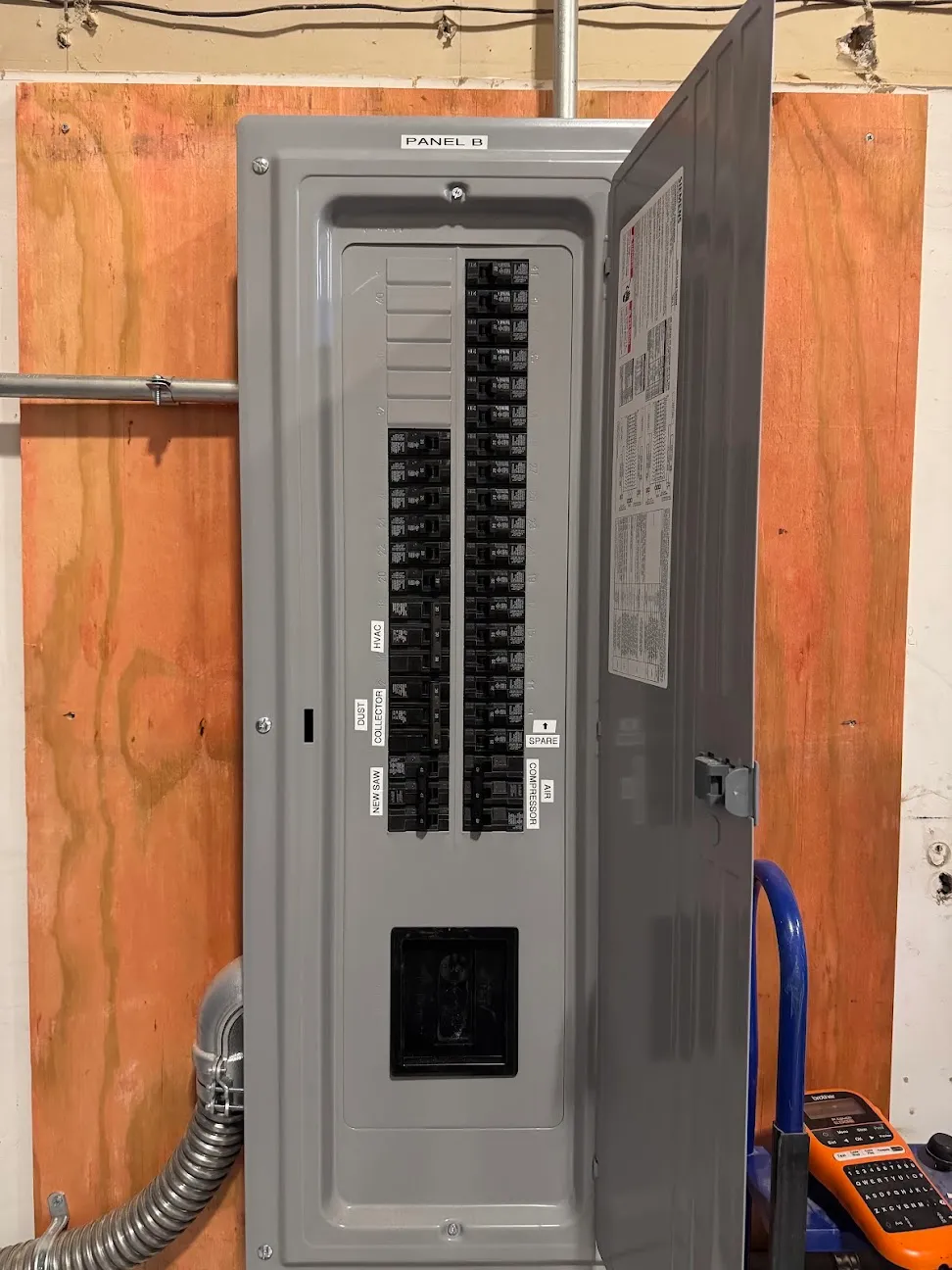 A large open panel board mounted on a plywood wall with the circuit directory visible