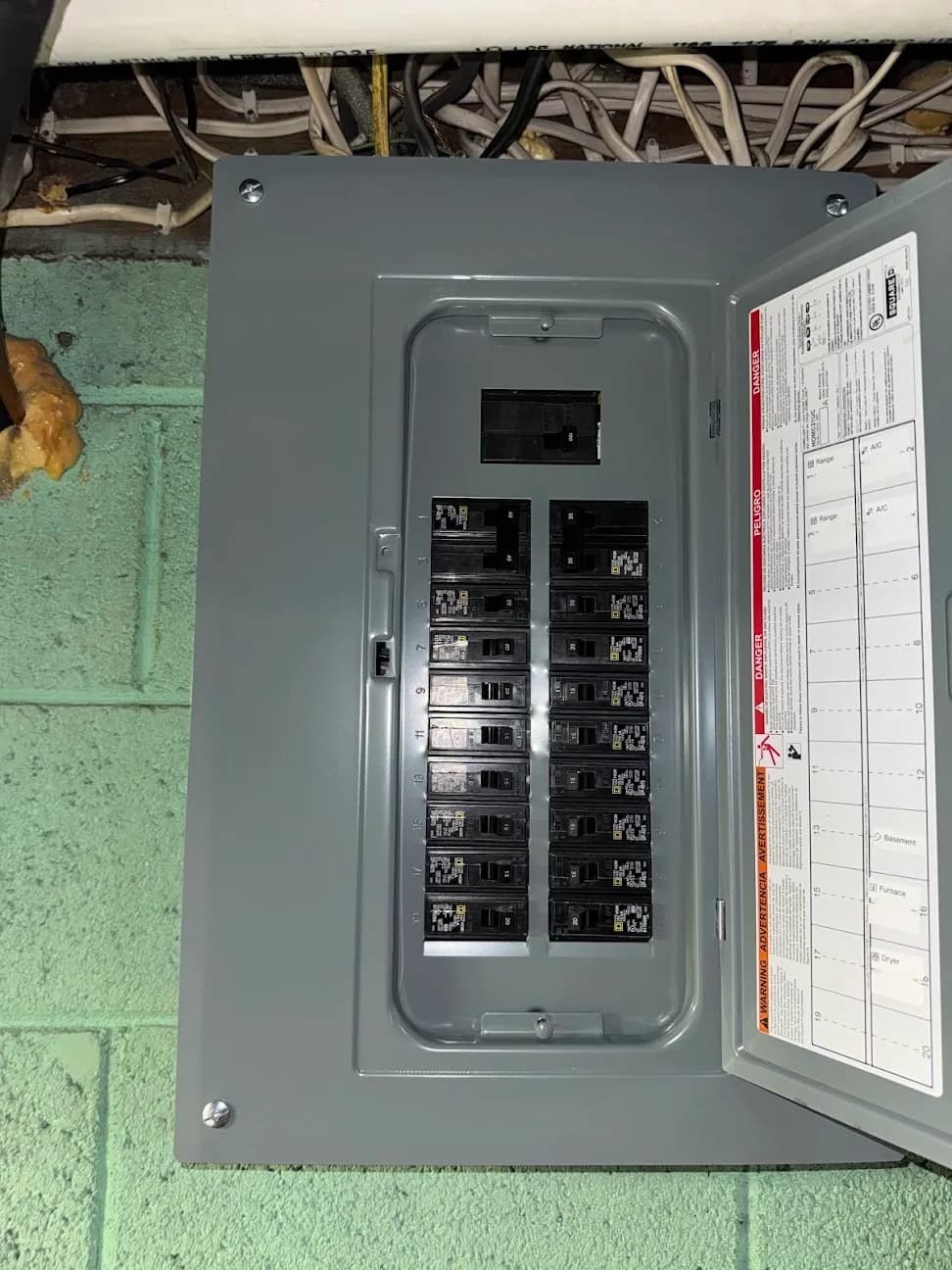 An open breaker panel mounted on a painted cinder block basement wall