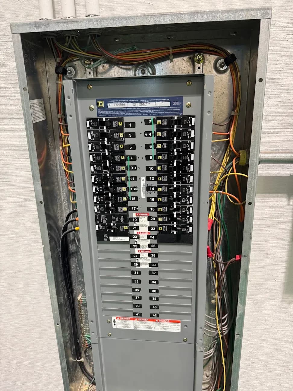 An open breaker panel with a full set of labeled circuits and colored wiring running out of the top