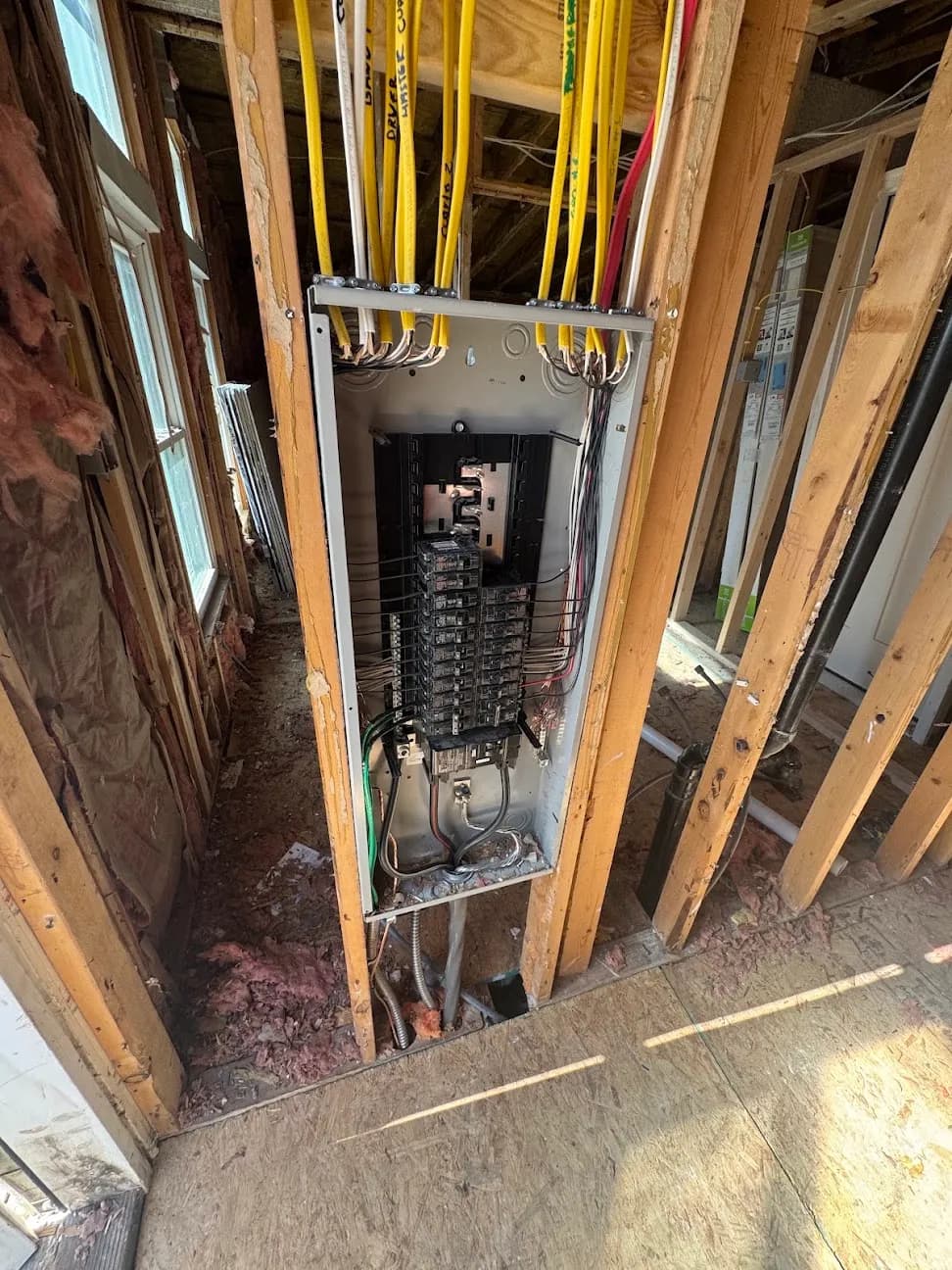 A breaker panel set into an open stud wall during rough-in, with yellow cable runs above it